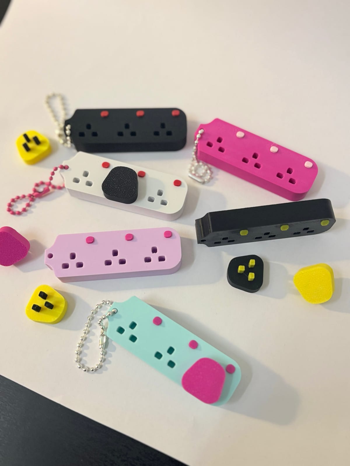 Extension plug keychains in mint, pink, black and white with yellow and black plug tops