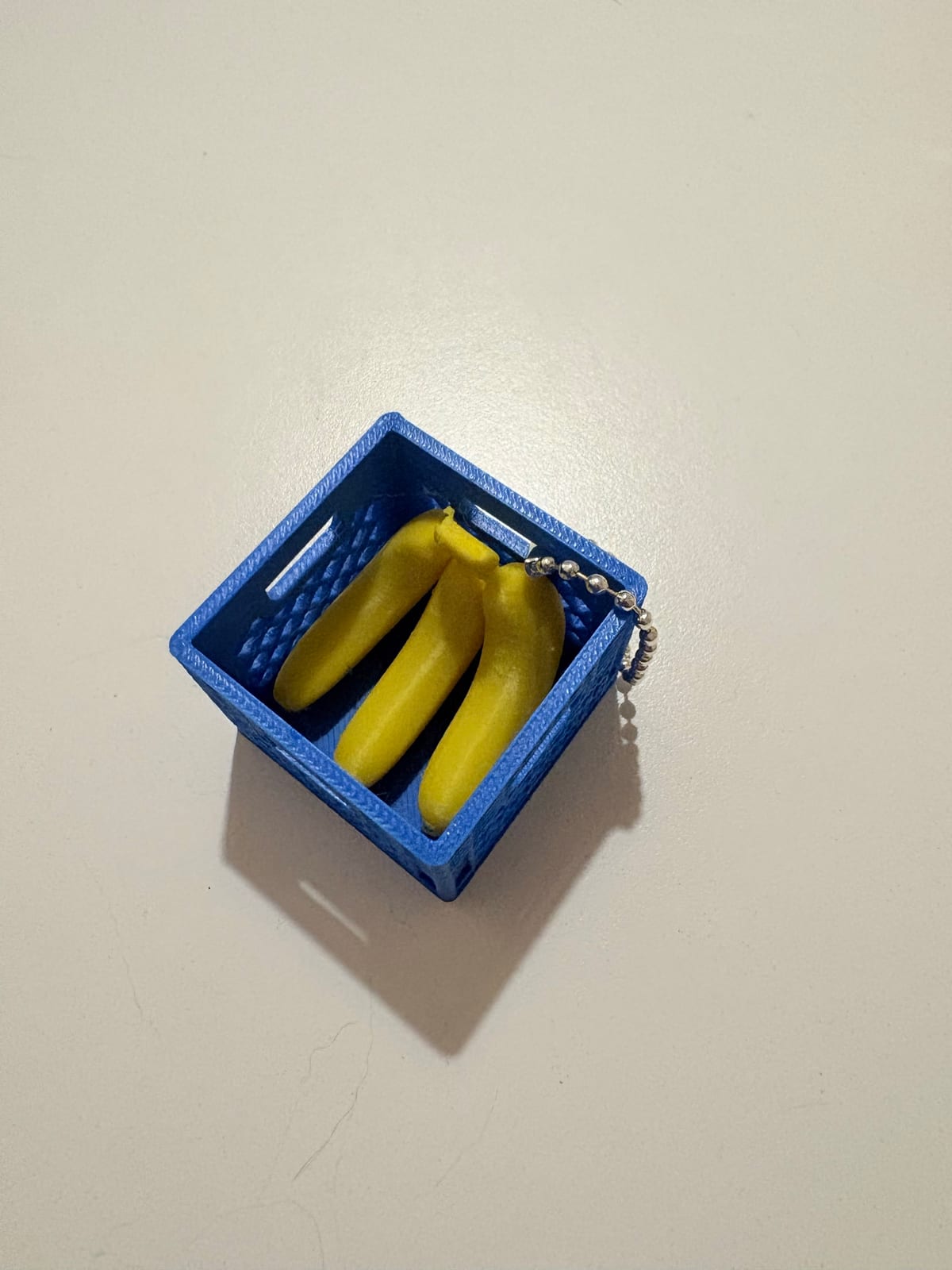 Blue fruit crate keychain filled with tiny yellow bananas