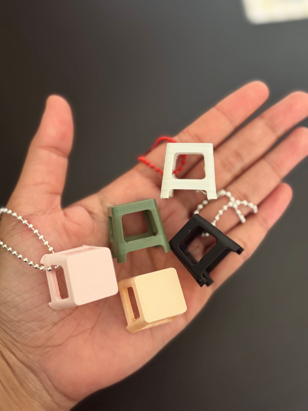 Kenduri stool keychains in pink, cream, green and red on an open hand