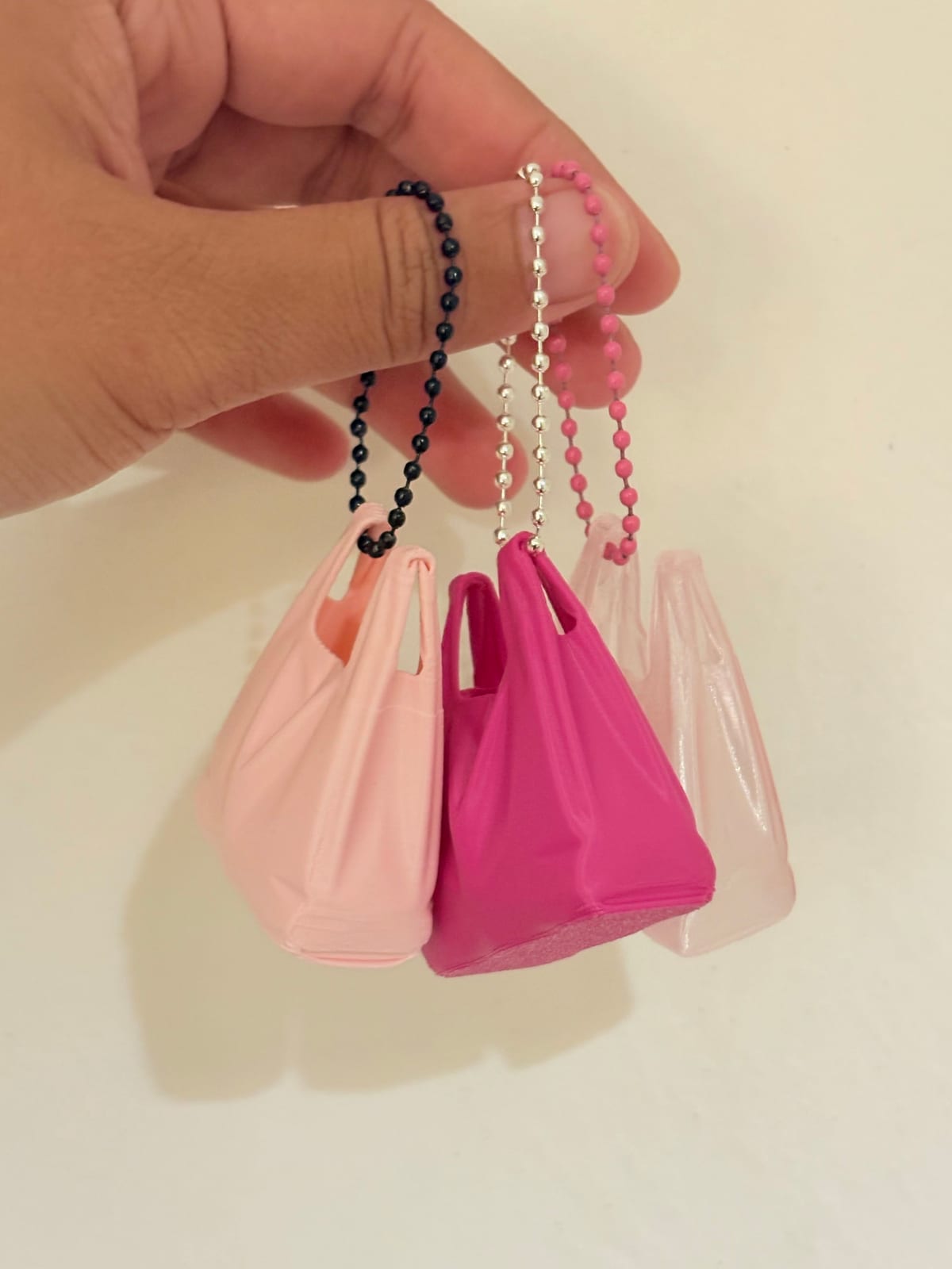 Pale pink and hot pink plastic bag keychains held up by their ball chains