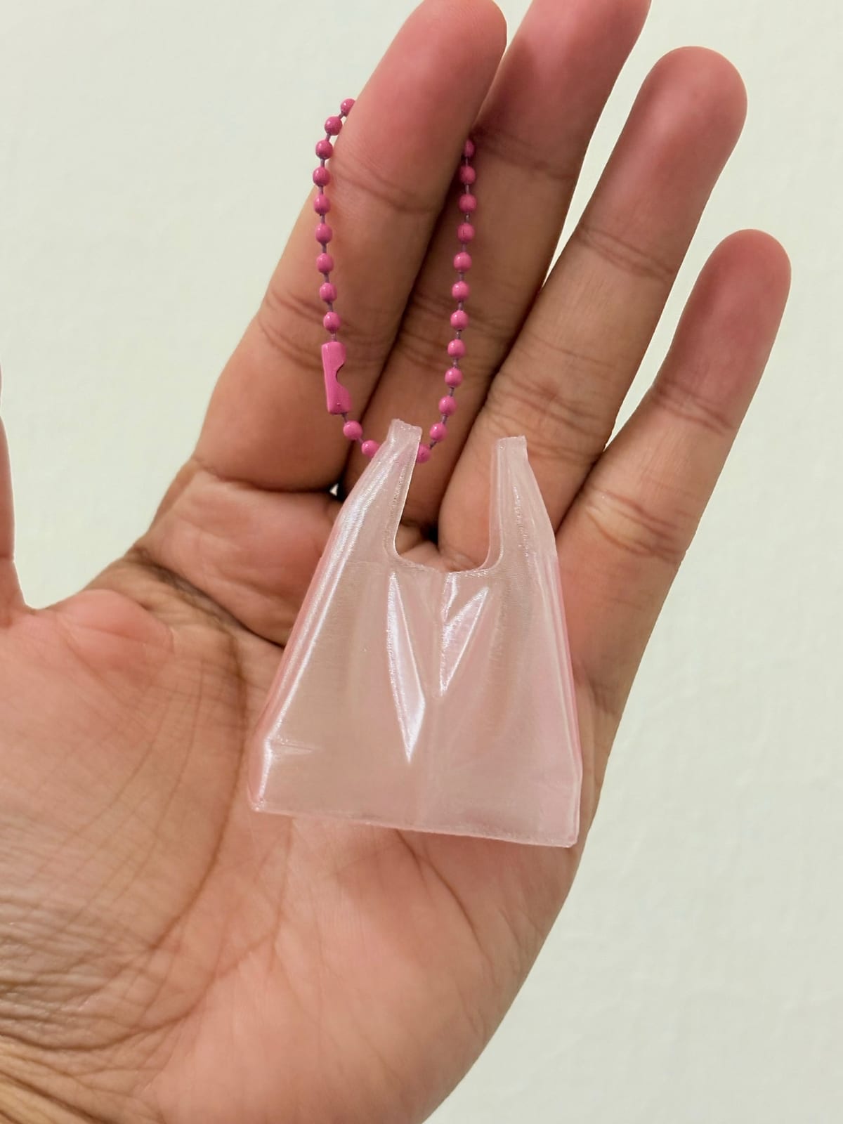 Pale pink plastic bag keychain resting on an open hand