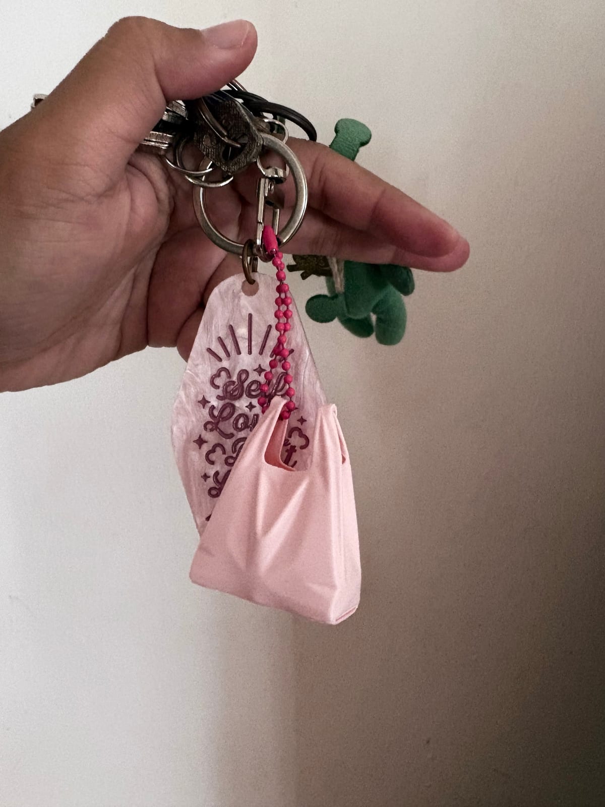 Pale pink plastic bag keychain hanging from a bag strap