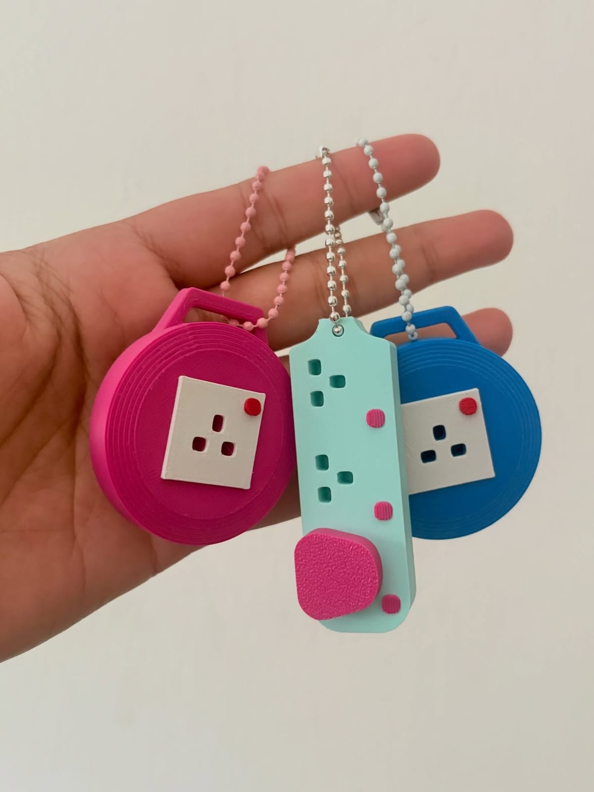 A pink round extension plug keychain next to a mint long one, held in a hand